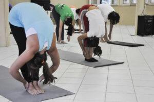 Mulheres se contorcem de pé em direção aos pés em atividade de yoga. 